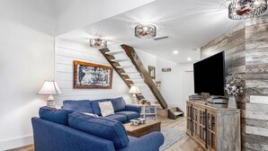 Uma sala de estar moderna com um sofá azul, uma escada de madeira e uma televisão de tela plana.