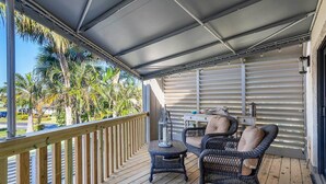 Uma área externa coberta com deck de madeira, móveis de vime e vista para palmeiras.