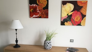 A bedroom with a wooden dresser, a bed, a lamp, and two paintings of flowers on the wall.