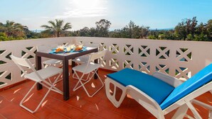 A terrace with a table set for two, white chairs, and a blue cushioned lounge chair.