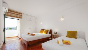 A hotel room with two beds, a wardrobe, a small table, and a window with a view.