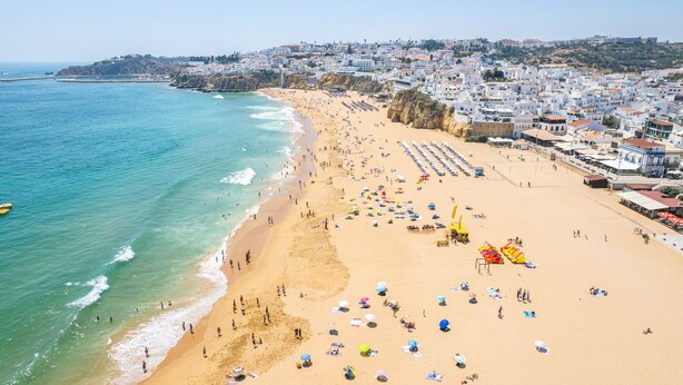 A coastal town with a wide sandy beach, numerous beach umbrellas, and a clear view of the sea.