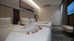 A hotel room with three beds, each with white linens and decorative swans. There is a large TV on the wall and a small seating area. - Ajm Mina Hotel (Makkah)
