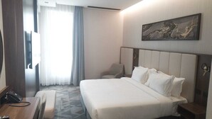 A hotel room with a large bed, a desk, a chair, a desk lamp, and a painting on the wall. - Ajm Mina Hotel (Makkah)