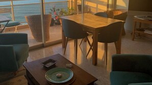 A spacious living area with a view of the sea, a dining table, and comfortable seating.