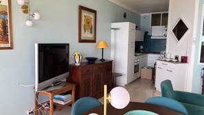 A compact living space with a TV, dining table, chairs, a kitchen area, and a dining table with a decorative plate.