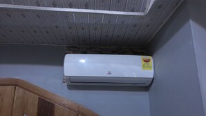 A white air conditioning unit mounted on a wall with a wooden staircase below. - Great Escape Inn Hotel  (Weija)