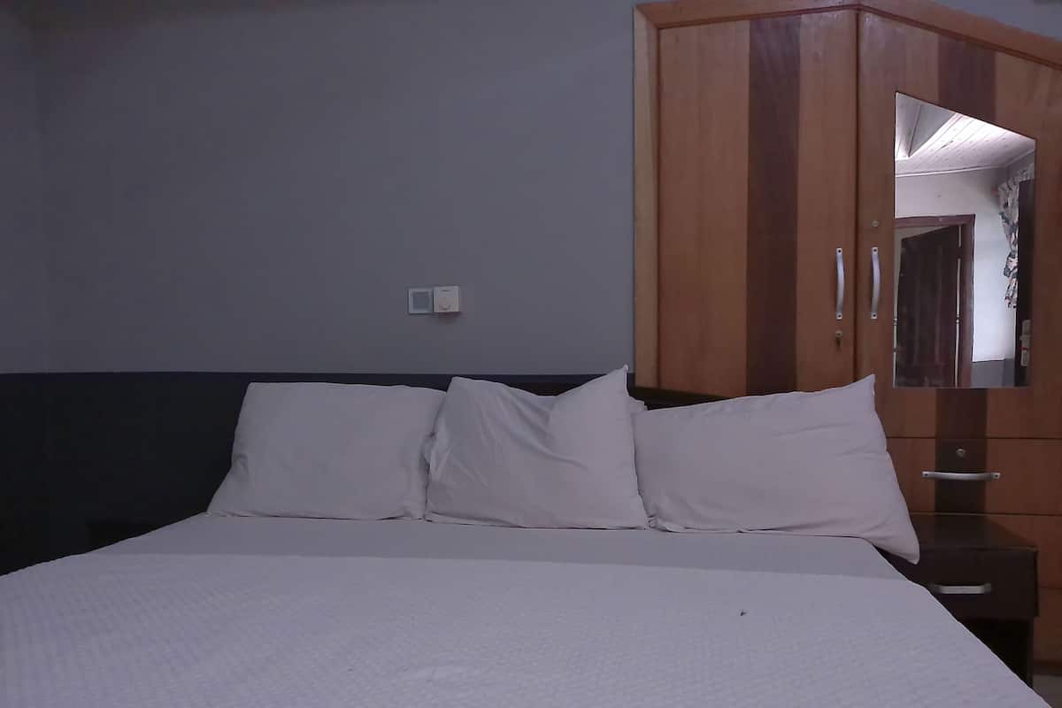 A bed with white linens and a headboard, a wooden wardrobe with a mirror, and a light switch on the wall.