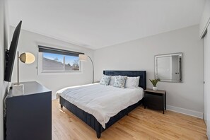A modern bedroom with a large bed, bedside tables, a TV, and a window with a view of the outside.