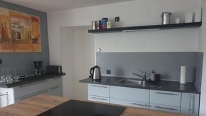 Una cucina moderna con un piano di lavoro nero, piano cottura integrato e lavello. Ci sono pensili con maniglie argentate e uno scaffale sopra il lavello con diversi oggetti.