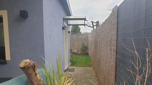 Un sentiero stretto che conduce a una casa con pareti azzurre e una recinzione in lamiera ondulata.