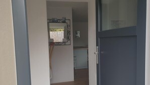 Un corridoio che conduce a una cucina, con una porta scura, uno specchio con cornice decorativa e un interruttore a muro.