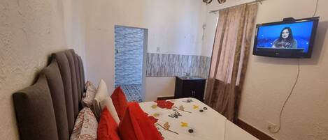 A hotel room with a bed, a television on the wall, a small table, and a window with curtains.