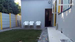 A small outdoor area with a grassy lawn, a stone pathway, and three white plastic chairs. - Neo & ruks guest house Boston (Cape Town)