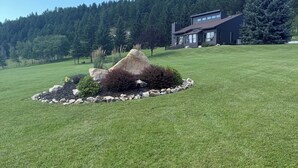 Une pelouse bien entretenue, agrémentée d’un massif rocheux central, avec une maison moderne en arrière-plan.