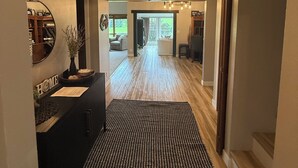 Un hall d’entrée spacieux, agrémenté d’un tapis à motifs noir et blanc, d’un lustre et offrant une vue sur un salon avec un canapé et une fenêtre.
