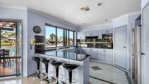 A modern kitchen with a large island, bar stools, and a view of a pool and outdoor area. - Riverside Manor (Sussex Inlet)