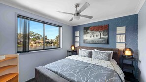 A bedroom with a bed, a ceiling fan, a window with a view of a lake, and a painting on the wall. - Riverside Manor (Sussex Inlet)