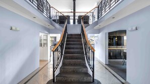 A staircase with a wooden handrail and metal balustrade, leading to a second floor with a balcony. - Riverside Manor (Sussex Inlet)