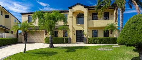 A multi-story residential building with a central arched entrance, surrounded by well-maintained lawns and palm trees.