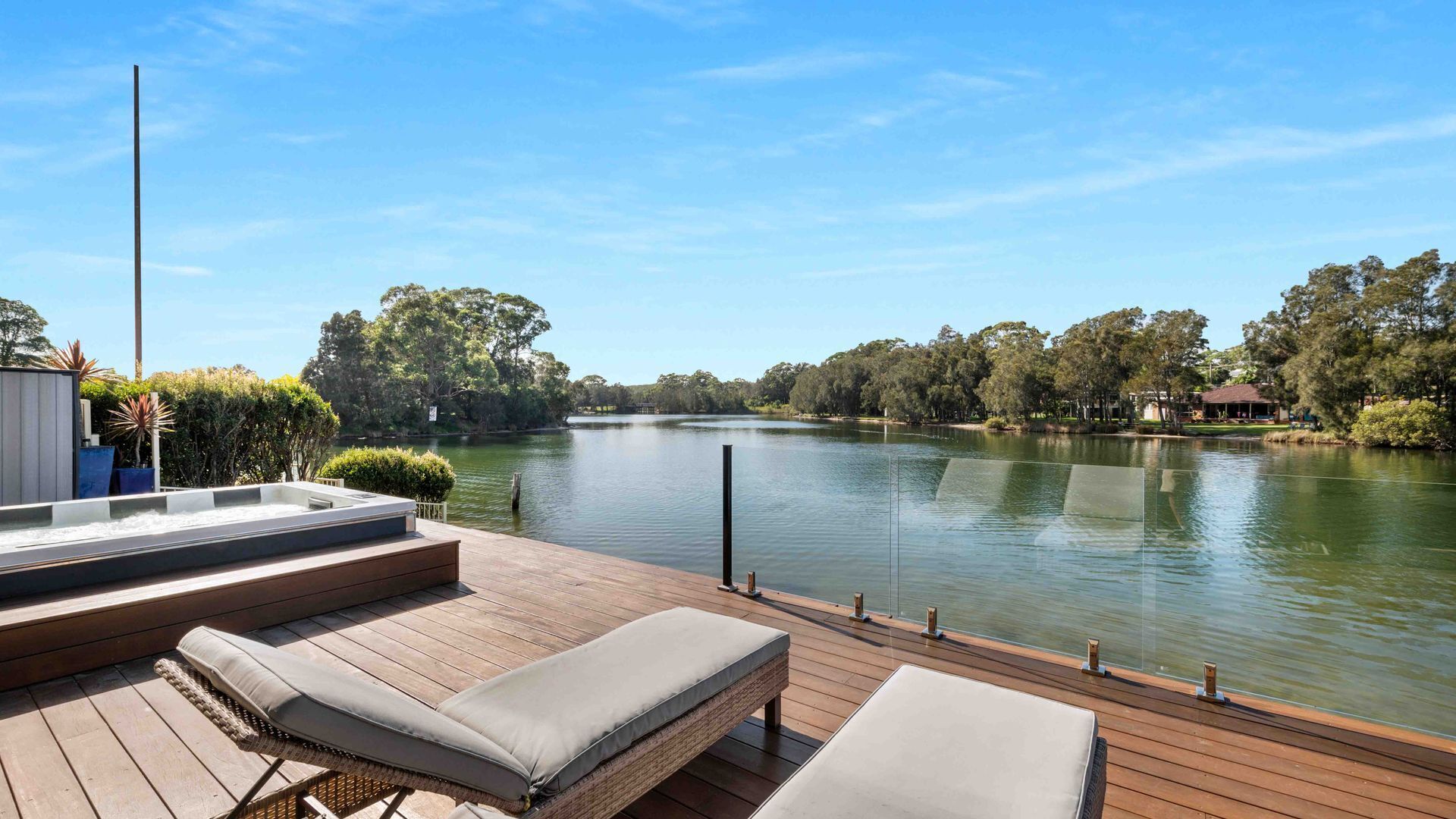 A wooden deck with lounge chairs and a view of a calm lake surrounded by trees.