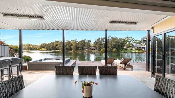 A modern outdoor dining area with a view of a lake and trees. - Riverside Manor (Sussex Inlet)