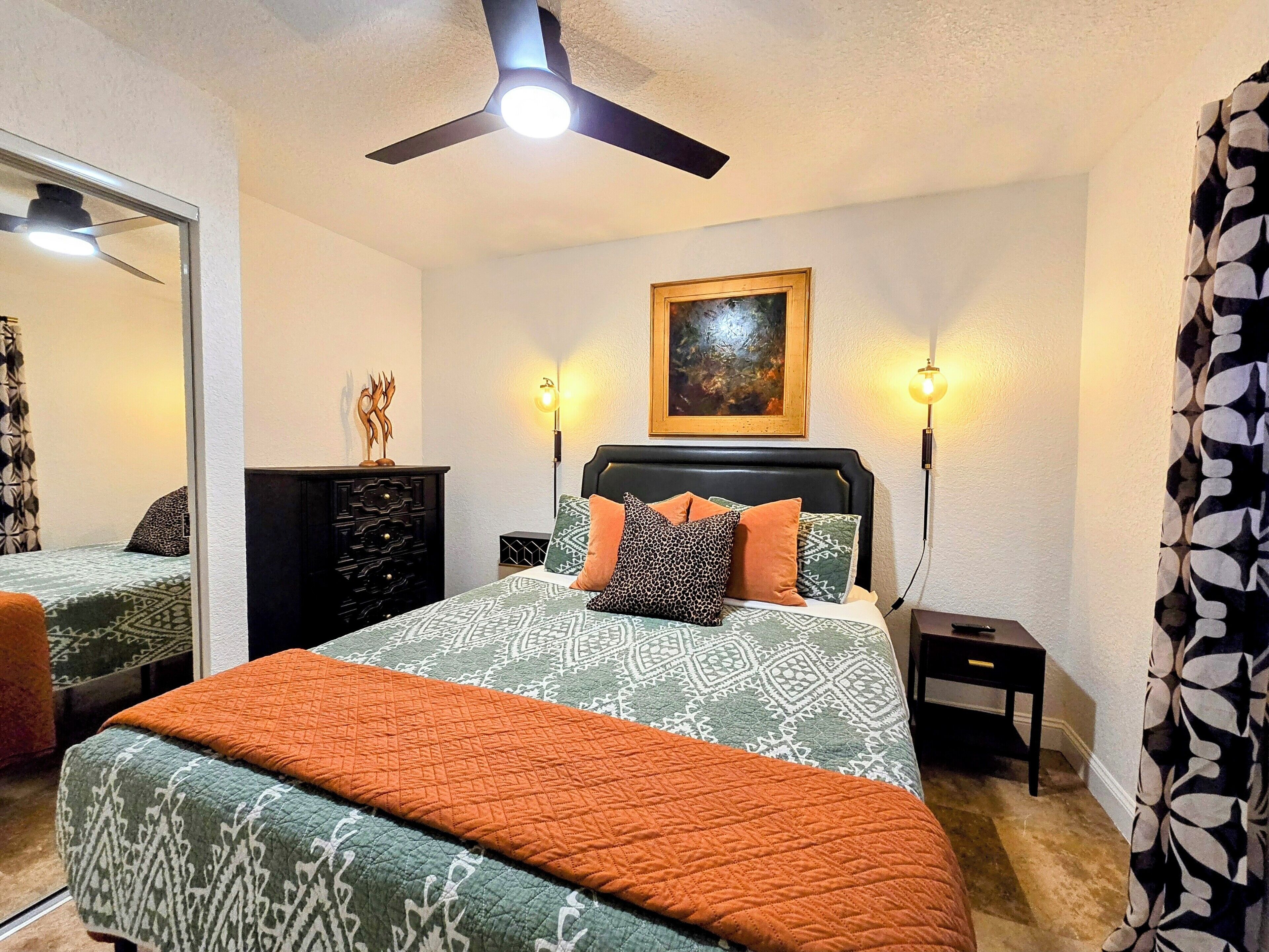 A bedroom with a bed, a dresser, a painting, and a ceiling fan.