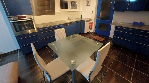 Une cuisine moderne avec des meubles de couleur bleu foncé, un four en acier inoxydable et une table à manger en verre, accompagnée de deux chaises.