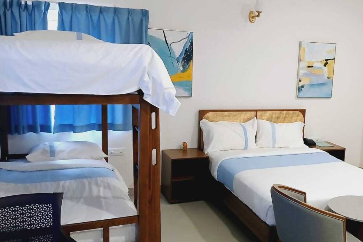 Ein Hotelzimmer mit einem Etagenbett, einem Einzelbett, einem kleinen Tisch, zwei Stühlen und Bildern an der Wand.
