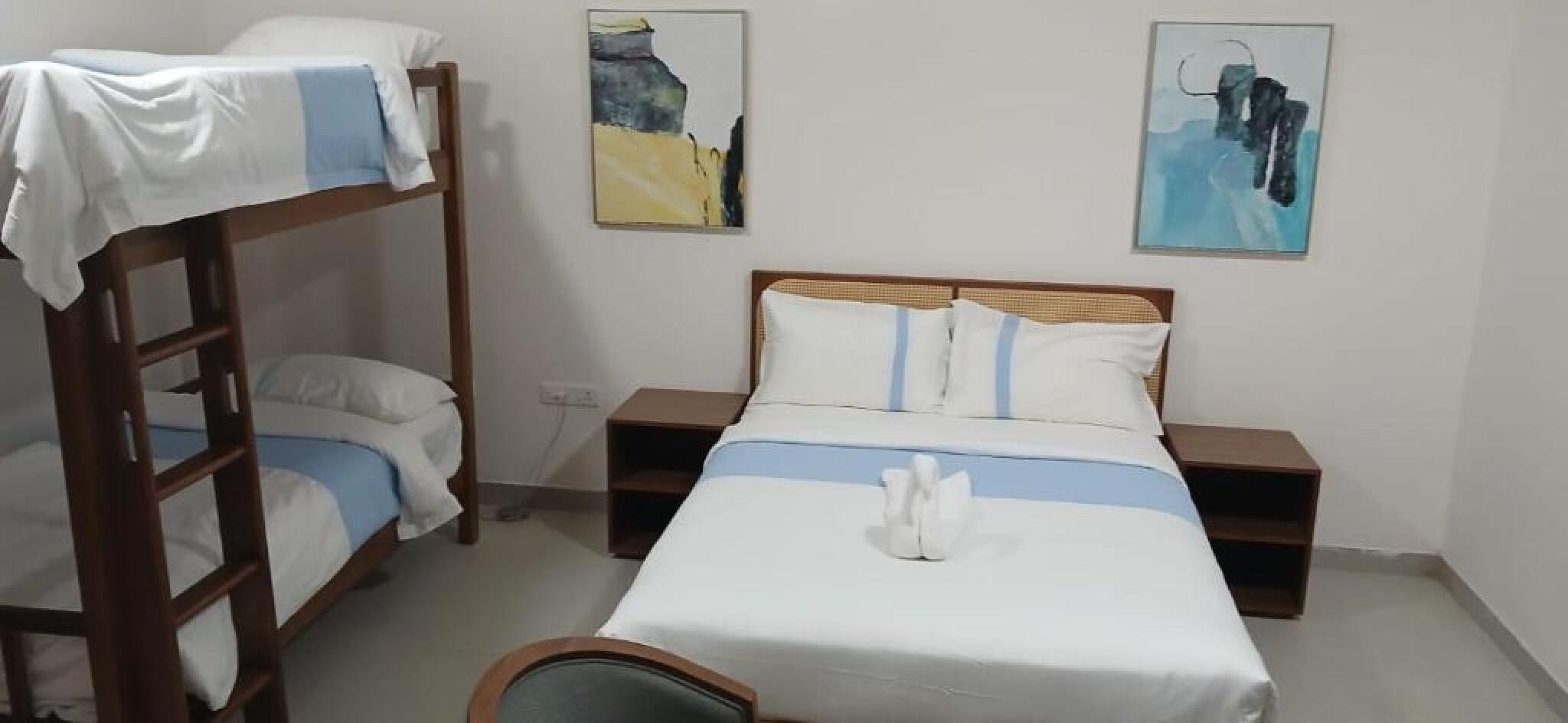 Ein Schlafraum mit Etagenbetten, einem Einzelbett, zwei Nachttischen und zwei Bildern an der Wand.