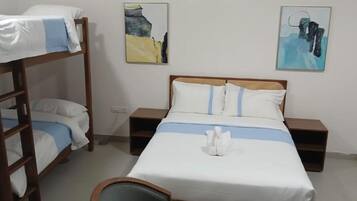 Ein Schlafraum mit Etagenbetten, einem Einzelbett, zwei Nachttischen und zwei Bildern an der Wand.