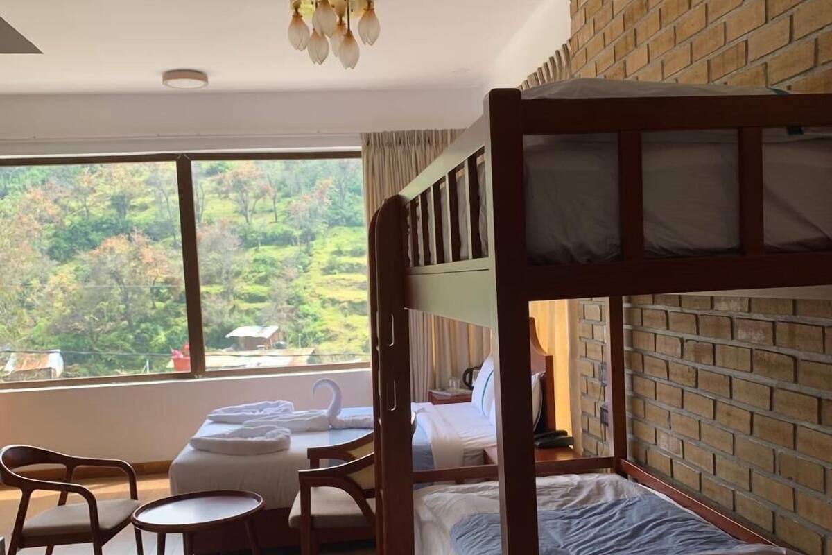 Ein Hotelzimmer mit einem Etagenbett, einem Schreibtisch, einem Stuhl und einem großen Fenster mit Blick auf Grünfläche.