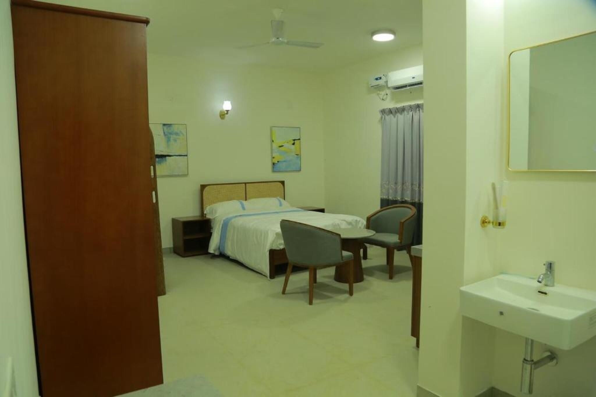 Habitación de hotel con cama, escritorio, silla, lavamanos y ventilador de techo.
