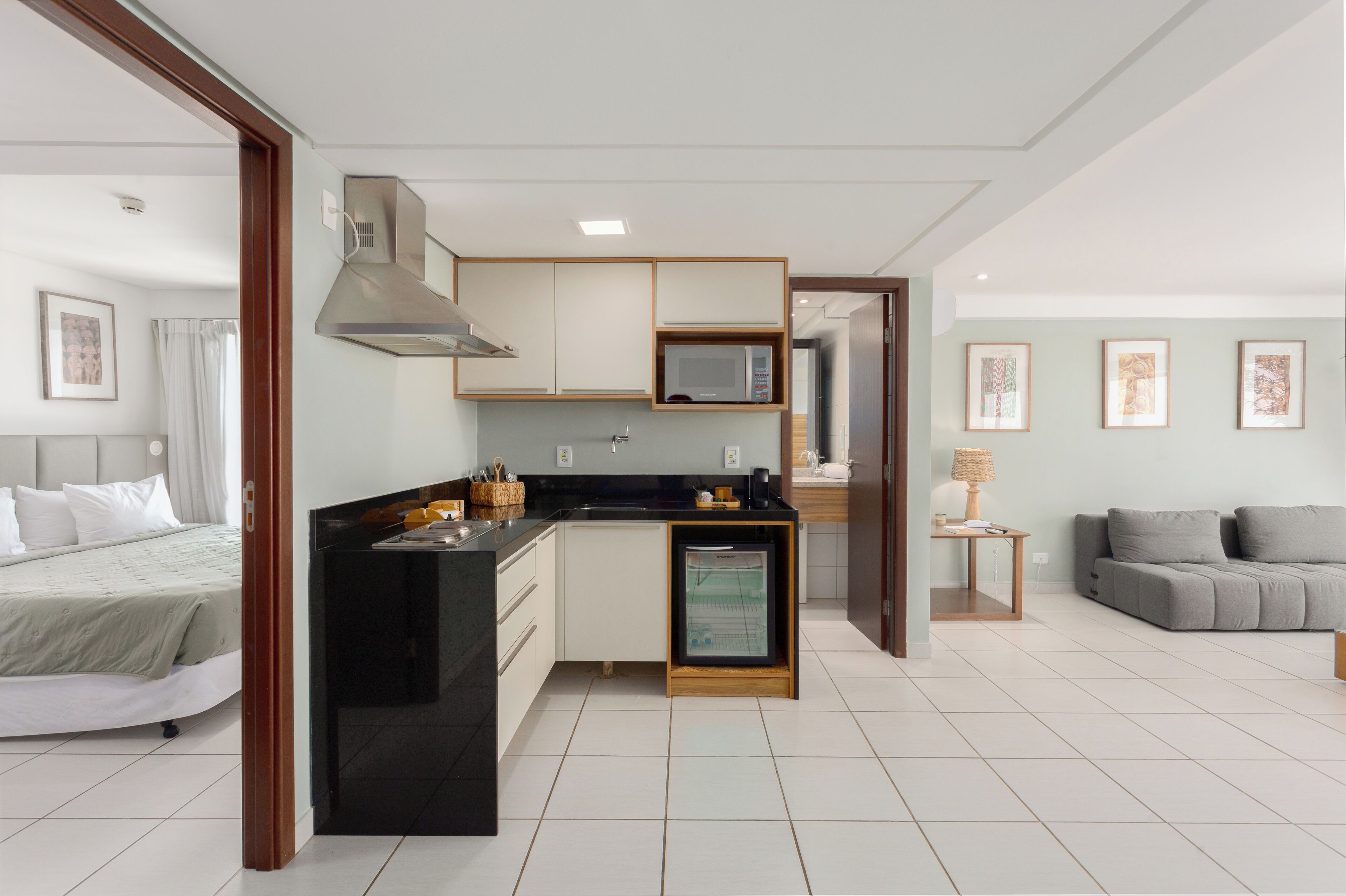 A compact hotel room with a kitchenette, a bed, a sofa, and a small dining area.
