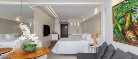A modern hotel room with a bed, a sofa, a dining table with chairs, a small kitchen area, and a large window.
