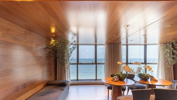 Una habitación moderna con techo de madera, ventanas amplias, una mesa redonda de madera y un sofá.