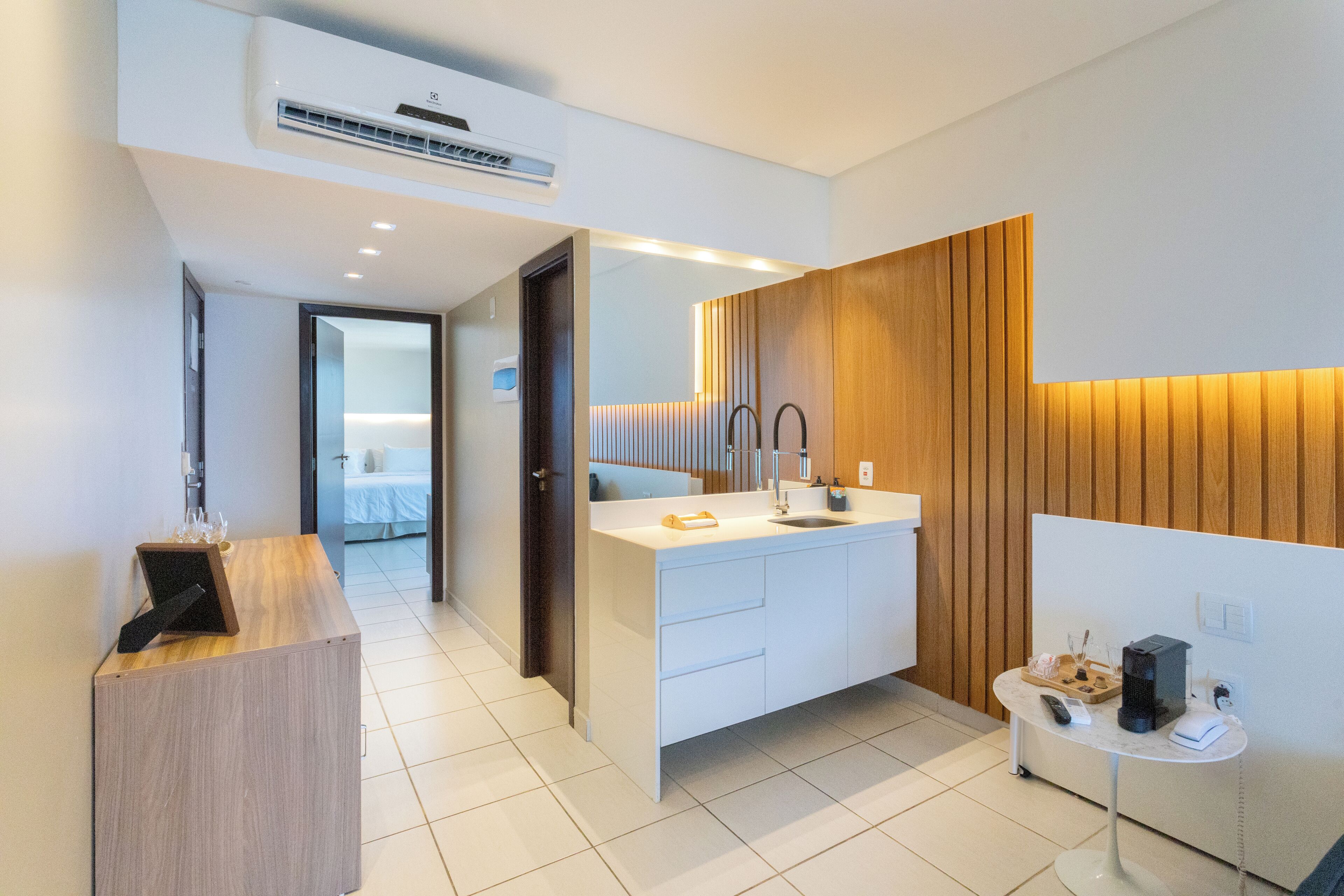 Un baño moderno con un mueble de tocador de madera, un espejo grande y una mesita con cafetera.