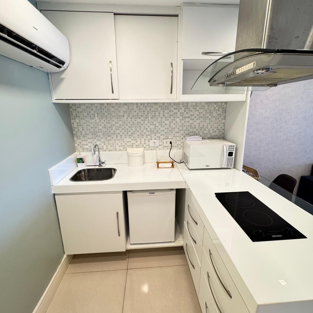 Une cuisine compacte avec des meubles blancs, un four à micro-ondes encastré, un évier et une cuisinière.
