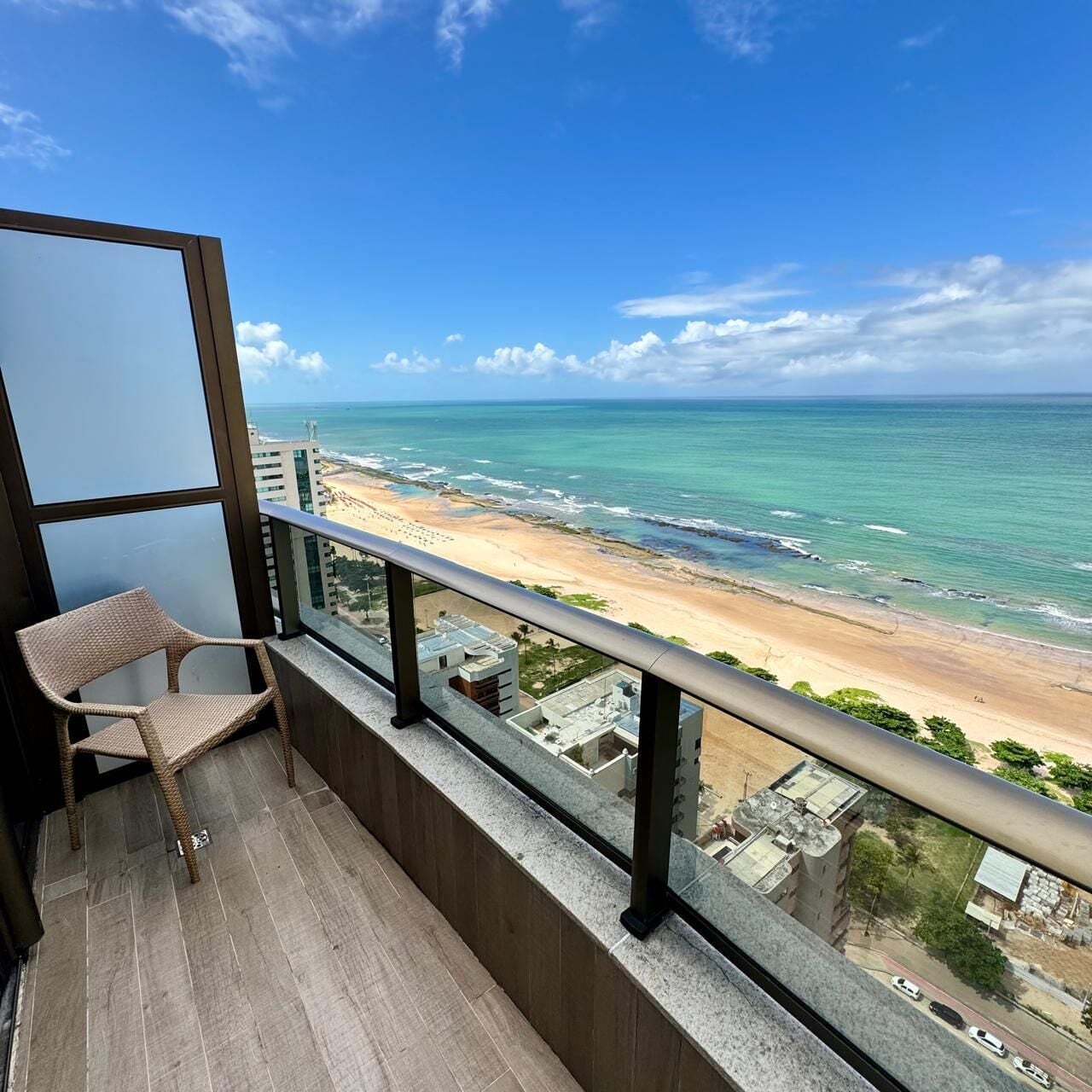 A balcony with a wicker chair, overlooking a beach with clear skies.
