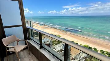 A balcony with a wicker chair, overlooking a beach with clear skies.