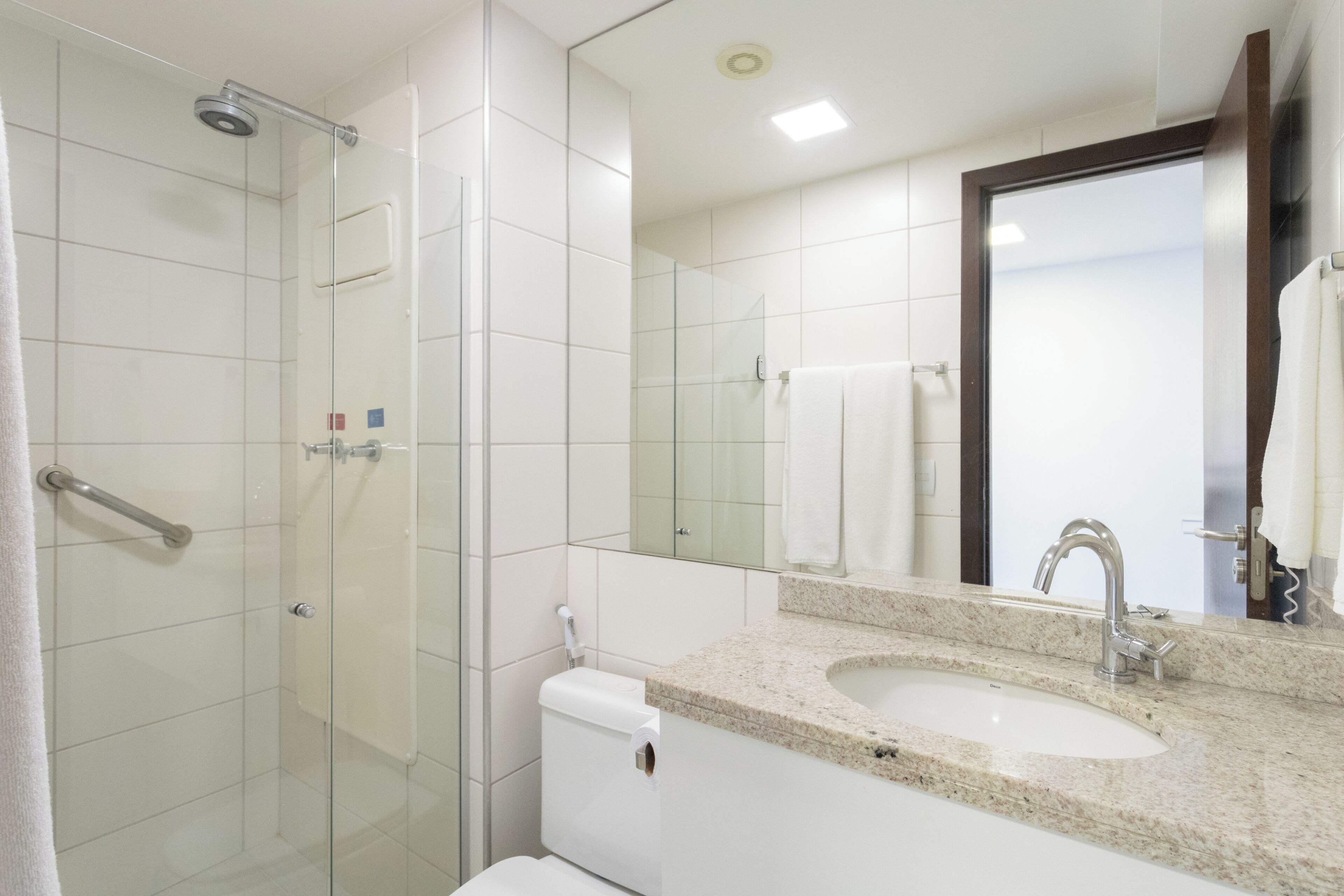 A modern bathroom with a glass shower enclosure, a white toilet, a sink with a granite countertop, and a large mirror.