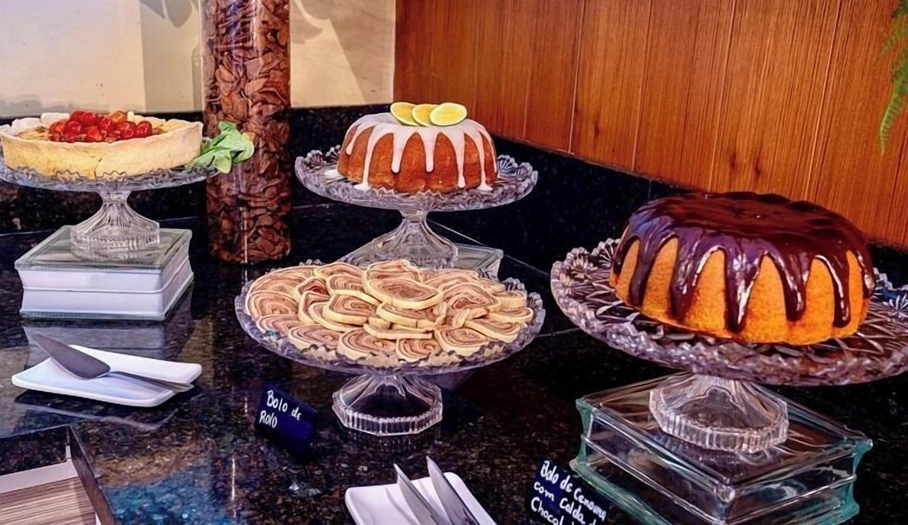 A variety of desserts on display in a glass case, including a chocolate-covered bundt cake, a cake with lemon slices, and a cake with a cream filling.