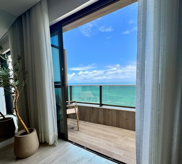 A balcony with a view of the ocean, a potted plant, and a chair.