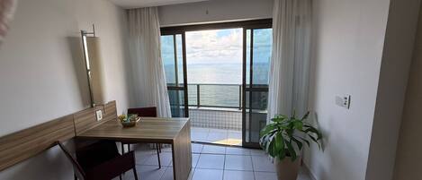 Ein Zimmer mit Holztisch, Stühlen, einer Topfpflanze und Meerblick durch große Fenster.