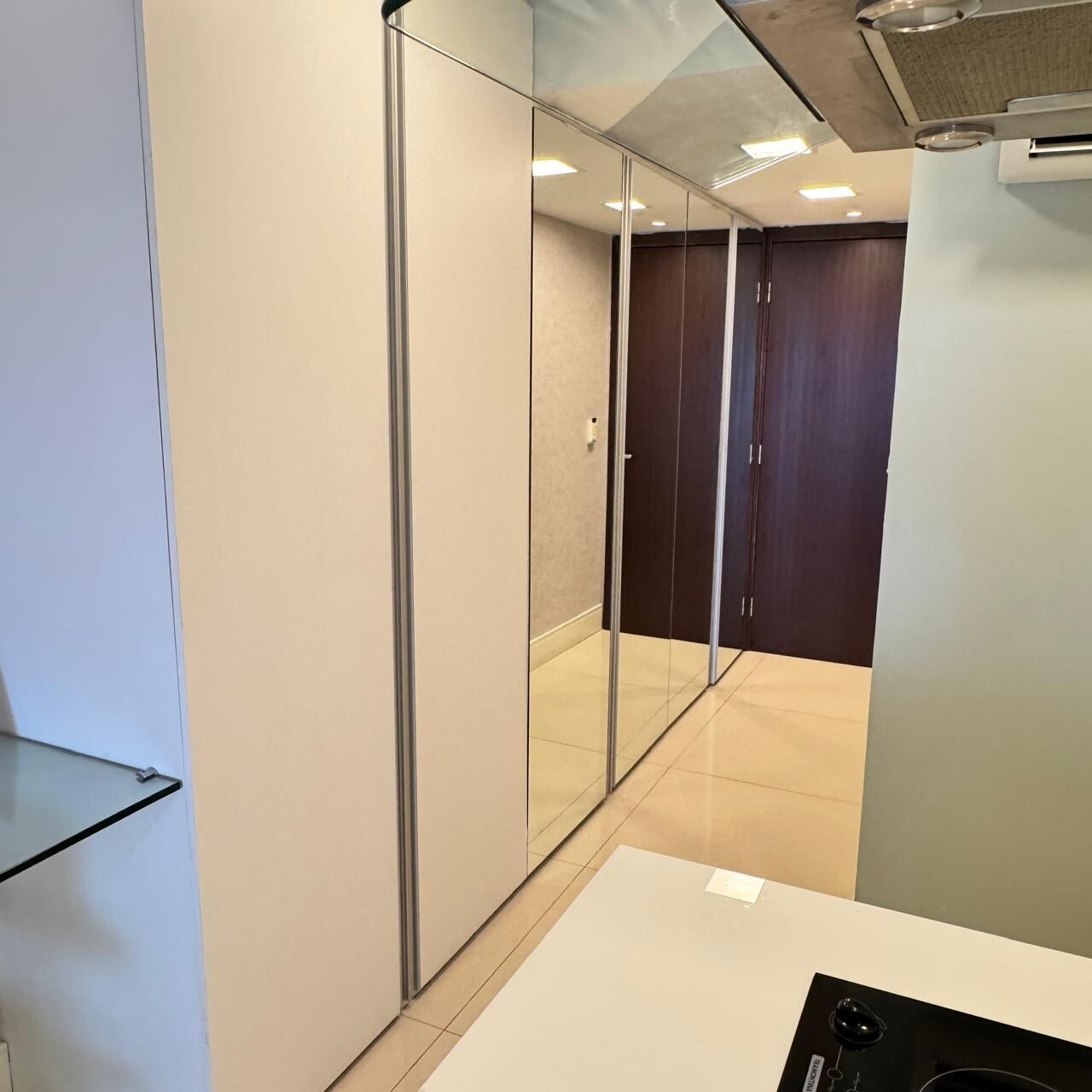 A modern hotel room with a glass partition, a white desk, and a dark wooden door.