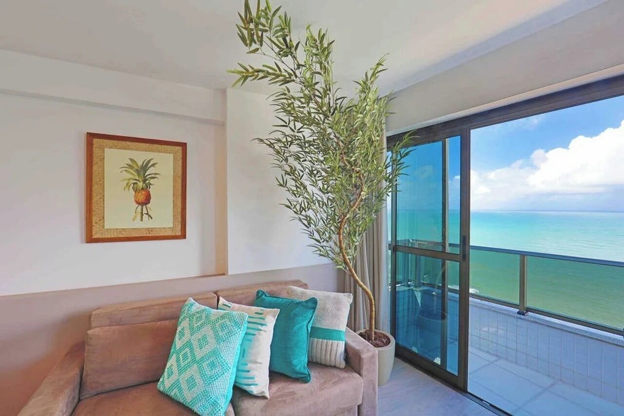 A balcony with a view of the ocean, a sofa with patterned cushions, and a framed picture on the wall.