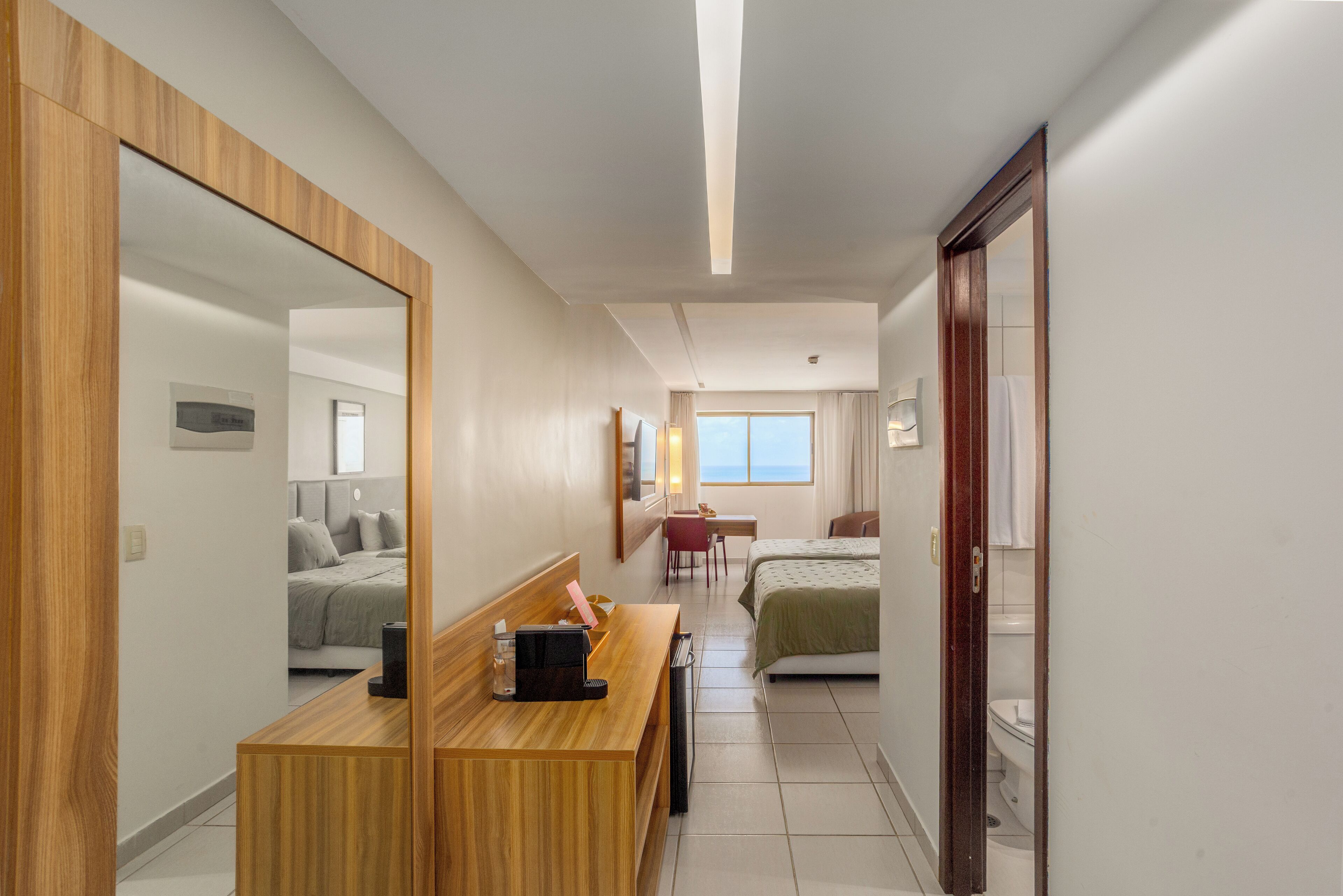 Une chambre d’hôtel avec un bureau en bois, un lit, une salle de bain et un grand miroir.