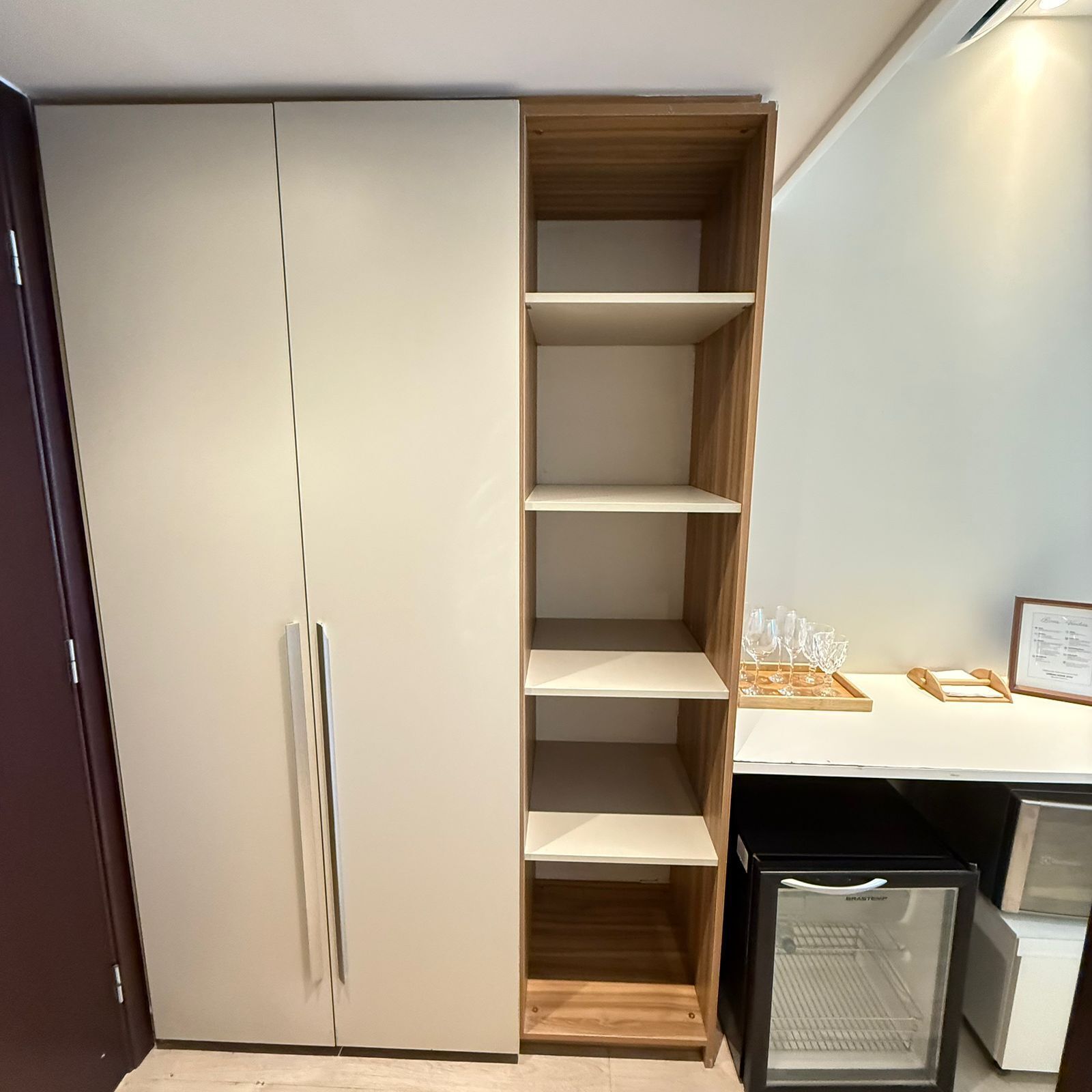 Een kitchenette met een ingebouwde koelkast, een houten kast en een aanrecht met een ingelijst certificaat.