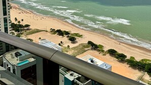 Une vue sur la plage depuis un immeuble de grande hauteur, avec un ciel dégagé et l’océan à l’horizon.