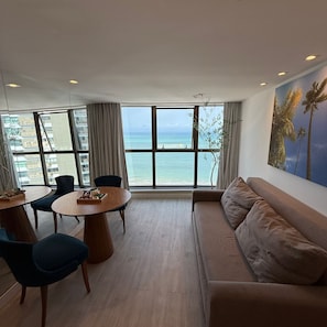 Una sala de estar moderna con un ventanal grande con vistas al mar, una mesa de comedor redonda y un sofá cómodo.